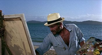 Movie still from “Age of Consent” (1969), directed by Michael Powell – A man wearing a straw hat is painting on the beach; Medium shot, Low angle
