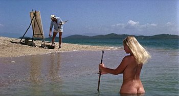 Movie still from “Age of Consent” (1969), directed by Michael Powell – A woman standing in the water next to a man on the beach; Wide shot, High angle