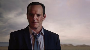 Movie still from “Agents of S.H.I.E.L.D.” (2013), created by Joss Whedon – A man wearing a suit and tie in front of a cloudy sky; Close Up shot, Low angle