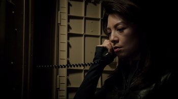 Movie still from “Agents of S.H.I.E.L.D.” (2013), created by Joss Whedon – A woman talking on a phone while wearing headphones; Close Up shot, High angle