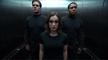 Movie still from “Agents of S.H.I.E.L.D.” (2013), created by Joss Whedon – A woman standing in front of two men in a elevator; Medium shot, Low angle