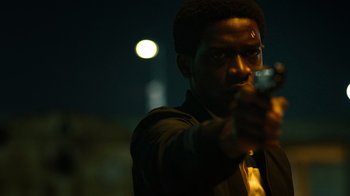 Movie still from “Snowfall” (2017), directed by Hiro Murai – A man is holding a gun in the dark at night; Close Up shot, Low angle