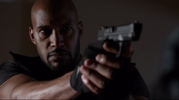 Movie still from “Agents of S.H.I.E.L.D.” (2013), created by Joss Whedon – A man holding a gun while wearing gloves; Close Up shot, Low angle