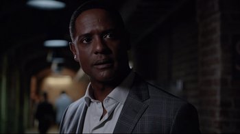 Movie still from “Agents of S.H.I.E.L.D.” (2013), created by Joss Whedon – A man wearing a suit and tie standing in a dark room; Close Up shot, Over the shoulder angle
