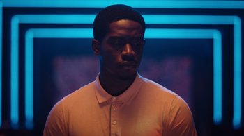Movie still from “Snowfall” (2017), directed by Hiro Murai – A man in a white shirt is standing in front of a blue background; Close Up shot, High angle