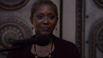 Movie still from “Agents of S.H.I.E.L.D.” (2013), created by Joss Whedon – A woman is speaking into a microphone in front of a wall; Close Up shot, Over the shoulder angle