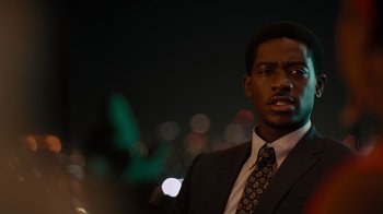 Movie still from “Snowfall” (2017), directed by Hiro Murai – A man wearing a suit and tie standing in front of a city skyline at night; Close Up shot, Low angle
