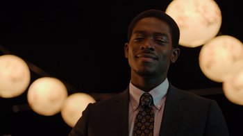 Movie still from “Snowfall” (2017), directed by Hiro Murai – A man in a suit and tie smiling for the camera; Close Up shot, Low angle