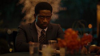 Movie still from “Snowfall” (2017), directed by Hiro Murai – A man sitting at a dinner table looking at the camera; Close Up shot, Over the shoulder angle