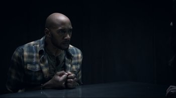 Movie still from “Agents of S.H.I.E.L.D.” (2013), created by Joss Whedon – A man sitting at a table with his hands clasped together; Medium shot, High angle