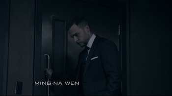Movie still from “Agents of S.H.I.E.L.D.” (2013), created by Joss Whedon – A man wearing a suit and tie standing in front of a door; Medium shot, Low angle