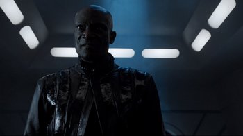 Movie still from “Agents of S.H.I.E.L.D.” (2013), created by Joss Whedon – A man in a leather jacket standing in a dark room; Close Up shot, Low angle
