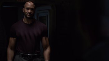 Movie still from “Agents of S.H.I.E.L.D.” (2013), created by Joss Whedon – A man in a maroon shirt is posing for a picture; Medium shot, Over the shoulder angle