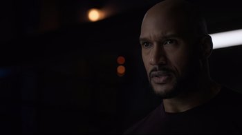 Movie still from “Agents of S.H.I.E.L.D.” (2013), created by Joss Whedon – A man with a bald head is looking at the camera; Close Up shot, Over the shoulder angle