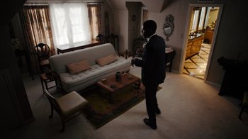 Movie still from “Snowfall” (2017), directed by Hiro Murai – A man standing in a living room holding a cell phone; Wide shot, High angle