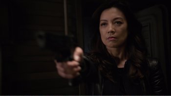 Movie still from “Agents of S.H.I.E.L.D.” (2013), created by Joss Whedon – A woman holding a gun in a dark room; Close Up shot, Over the shoulder angle
