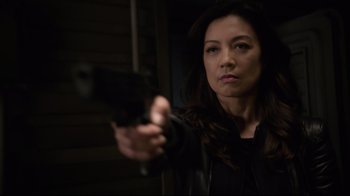 Movie still from “Agents of S.H.I.E.L.D.” (2013), created by Joss Whedon – A woman holding a gun in a dark room; Close Up shot, Over the shoulder angle