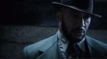 Movie still from “Agents of S.H.I.E.L.D.” (2013), created by Joss Whedon – A man in a suit and hat is looking at the camera; Close Up shot, Low angle