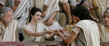 Movie still from “Agora” (2009), directed by Alejandro Amenábar – A woman holding a piece of bread in front of a group of people; Medium shot, Over the shoulder angle