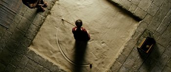 Movie still from “Agora” (2009), directed by Alejandro Amenábar – A person sitting on the ground holding a hose; Wide shot, Overhead angle