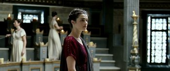 Movie still from “Agora” (2009), directed by Alejandro Amenábar – A woman standing in front of a staircase wearing a red dress; Medium shot, Over the shoulder angle