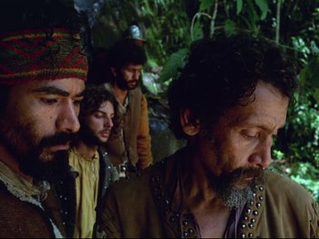 Movie still from “Aguirre, the Wrath of God” (1972), directed by Werner Herzog – A group of men standing next to each other in the woods; Medium shot, Low angle