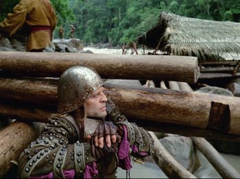 Movie still from “Aguirre, the Wrath of God” (1972), directed by Werner Herzog – A man wearing a helmet and holding a sword; Wide shot, Low angle