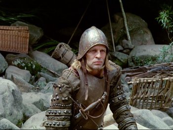 Movie still from “Aguirre, the Wrath of God” (1972), directed by Werner Herzog – A man dressed as a medieval knight sitting on rocks; Medium shot, Low angle