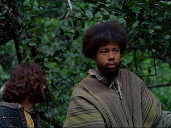Movie still from “Aguirre, the Wrath of God” (1972), directed by Werner Herzog – A man with a beard is standing next to another man in a forest; Medium shot, Low angle