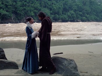 Movie still from “Aguirre, the Wrath of God” (1972), directed by Werner Herzog – A man and a woman standing on a rock near a body of water; Wide shot, High angle