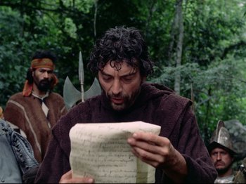 Movie still from “Aguirre, the Wrath of God” (1972), directed by Werner Herzog – A man in a brown robe looking at a piece of paper in front of another man; Close Up shot, Over the shoulder angle