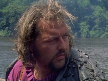 Movie still from “Aguirre, the Wrath of God” (1972), directed by Werner Herzog – A person wearing a purple shirt near a body of water; Close Up shot, Low angle