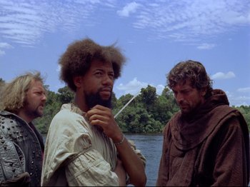 Movie still from “Aguirre, the Wrath of God” (1972), directed by Werner Herzog – A group of men standing next to a body of water; Medium shot, Over the shoulder angle