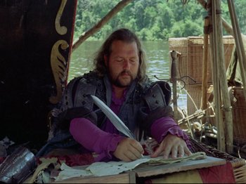 Movie still from “Aguirre, the Wrath of God” (1972), directed by Werner Herzog – A man sitting in a boat writing on a piece of paper; Medium shot, High angle