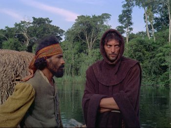 Movie still from “Aguirre, the Wrath of God” (1972), directed by Werner Herzog – Two men standing next to each other near a body of water; Medium shot, Low angle