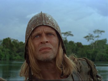 Movie still from “Aguirre, the Wrath of God” (1972), directed by Werner Herzog – A person with long hair wearing a helmet; Close Up shot, Low angle