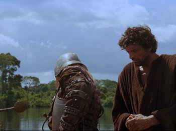 Movie still from “Aguirre, the Wrath of God” (1972), directed by Werner Herzog – A man in a brown robe standing next to another man in a brown robe; Medium shot, Over the shoulder angle