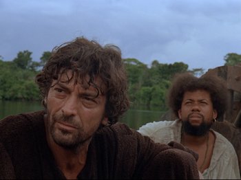 Movie still from “Aguirre, the Wrath of God” (1972), directed by Werner Herzog – Two men sitting next to a body of water; Close Up shot, Low angle