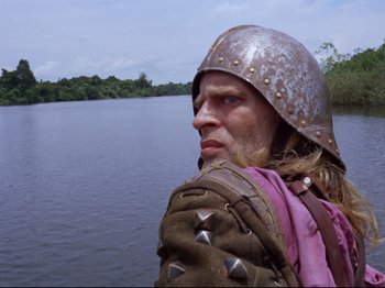 Movie still from “Aguirre, the Wrath of God” (1972), directed by Werner Herzog – A man with a helmet on looking at the camera; Medium shot, Low angle