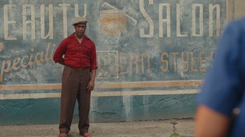 Movie still from “A League of Their Own” (2022), created by Abbi Jacobson – A man standing in front of an advertisement; Medium shot, Low angle