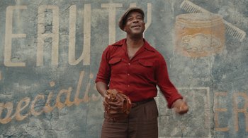 Movie still from “A League of Their Own” (2022), created by Abbi Jacobson – A man holding a baseball glove in his hand; Medium shot, Low angle