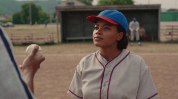 Movie still from “A League of Their Own” (2022), created by Abbi Jacobson – A woman in a baseball uniform is holding a ball; Medium shot, Over the shoulder angle