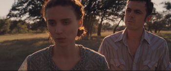 Movie still from “Ain't Them Bodies Saints” (2013), directed by David Lowery – A woman standing next to a man on a field; Close Up shot, Over the shoulder angle