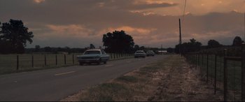 Movie still from “Ain't Them Bodies Saints” (2013), directed by David Lowery – A group of cars driving down a road near a tree; Extreme Wide shot, Low angle