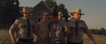 Movie still from “Ain't Them Bodies Saints” (2013), directed by David Lowery – A group of people standing next to each other in front of a building; Medium shot, Low angle
