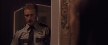 Movie still from “Ain't Them Bodies Saints” (2013), directed by David Lowery – A man in a police uniform looking in a mirror; Medium shot, Over the shoulder angle