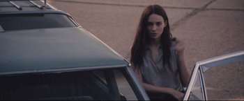 Movie still from “Ain't Them Bodies Saints” (2013), directed by David Lowery – A woman standing in front of a parked car; Medium shot, Over the shoulder angle