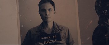 Movie still from “Ain't Them Bodies Saints” (2013), directed by David Lowery – A man holding up a license plate while standing in front of a brick wall; Close Up shot, Low angle