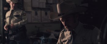 Movie still from “Ain't Them Bodies Saints” (2013), directed by David Lowery – A man wearing a cowboy hat in a dark room; Close Up shot, Over the shoulder angle