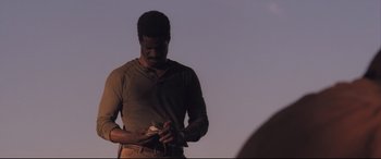 Movie still from “Ain't Them Bodies Saints” (2013), directed by David Lowery – A man standing in the middle of a field holding something; Medium shot, Low angle